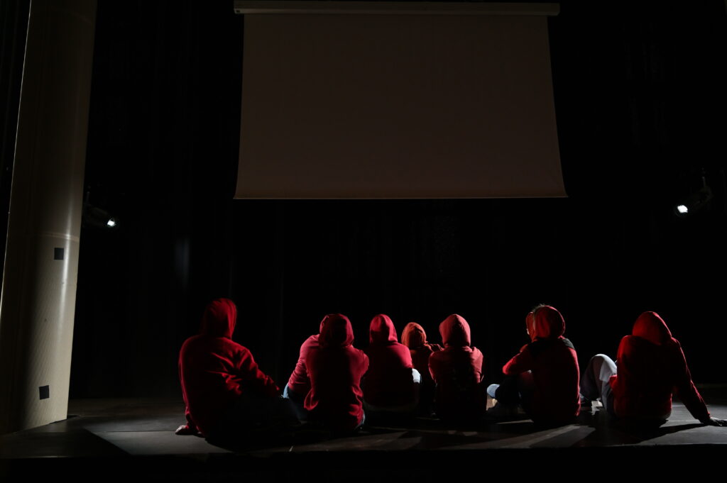 Les comédien.nes assis dans la demi-obscurité sur le plateau